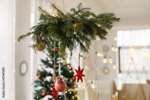 Spruce branches with red christmas ornaments above the table and Christmas tree on background