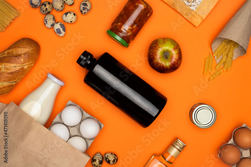 Eggs and bottle of milk in paper eco bag. Spaghetti, bread, quail eggs, beans, tomato paste on orange background. Healthy food, delivery, donation concept. Food stock for quarantine. Top view, flatly.