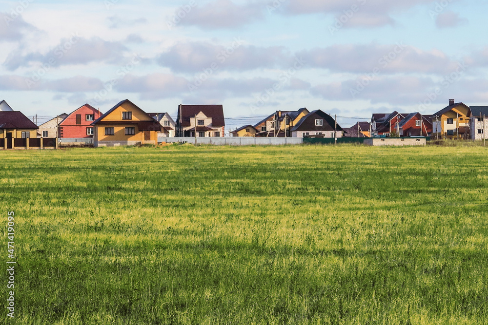 A lawn with green grass all the way to the horizon. Horizontal landscape of a flat field with fresh spring grass. Village, country houses, SNT, on the background of fields and trees. A lawn with green grass all the way to the horizon. Horizontal landscape of a flat field with fresh spring grass. Village, country houses, SNT, on the background of fields and trees.