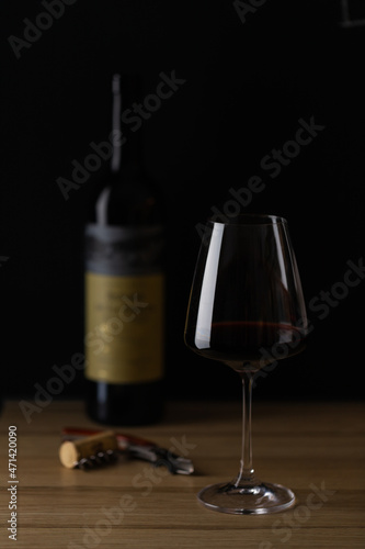 The wine is poured into a glass and stands on the table, next to the wine bottle, corkscrew and cork. Dark background. Front view.
