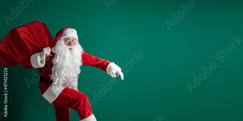 Tablou pe pânză Surprised Santa Claus sneaking while carrying huge red sack with presents on gre