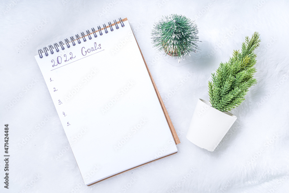 2022 new year goals concept. Year plan and action list on notepad with holiday decoration, latte coffee cup on white fluffy background flatlay top view copy space 2022 new year goals concept. Year plan and action list on notepad with holiday decoration, latte coffee cup on white fluffy background flatlay top view copy space