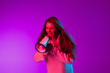 Portrait of young pretty girl shouting at megaphone isolated over purple studio background in neon light.