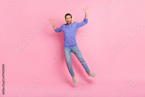 Full length photo of brunet cool millennial guy jump wear headphones blue pullover jeans sneakers isolated on pink background