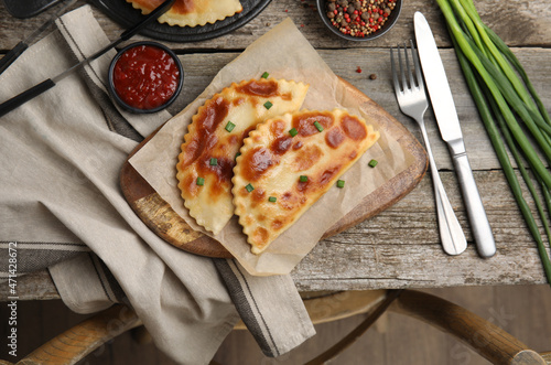 Delicious fried chebureki with ketchup served on wooden table, flat lay photo