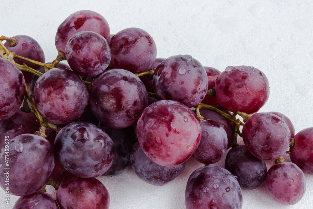 Purple grapes on a white background with drops on the fruits Purple grapes on a white background with drops on the fruits