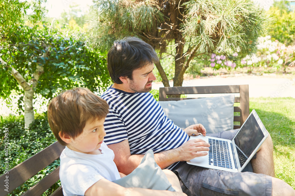 Vater und Sohn mit Laptop Computer im Garten im Sommer
