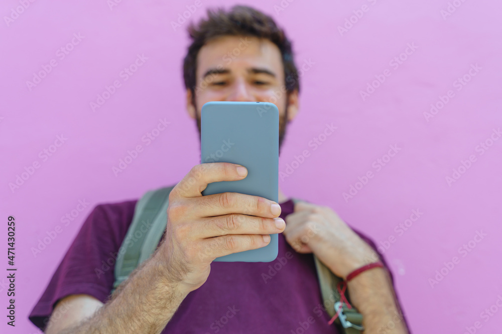 front view of unrecognizable man holding a phone on pink background. Horizontal view of latin american man using technology isolated on pink wall. People and travel concept. front view of unrecognizable man holding a phone on pink background. Horizontal view of latin american man using technology isolated on pink wall. People and travel concept.