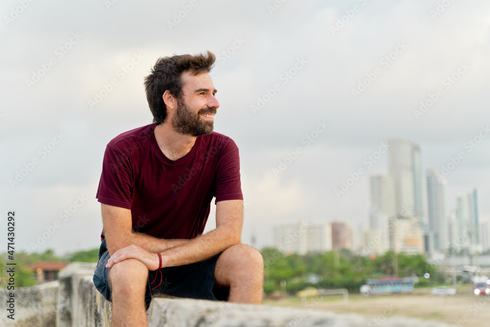 Side view of caucasian man traveling in Colombia. Horizontal view of man sightseeing sit in ancient wall of Cartagena de Indias. Travel to Colombia concept. Side view of caucasian man traveling in Colombia. Horizontal view of man sightseeing sit in ancient wall of Cartagena de Indias. Travel to Colombia concept.