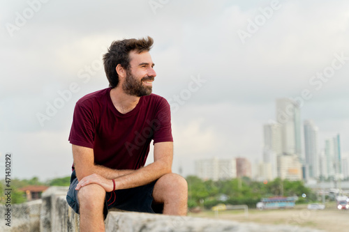 Side view of caucasian man traveling in Colombia. Horizontal view of man sightseeing sit in ancient wall of Cartagena de Indias. Travel to Colombia concept.