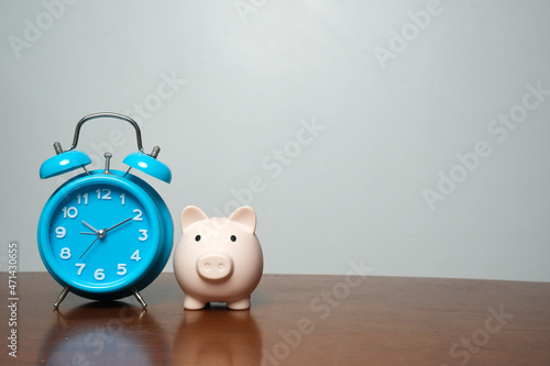 A picture of piggybank with clock on the table and copyspace. Saving and time value of money.