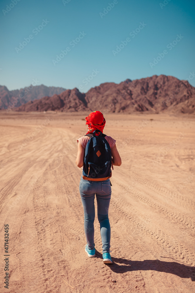 Traveler admiring Sinai Desert and mountains. Tourist woman with backpack wearing scarf on head walking on sand. Traveler admiring Sinai Desert and mountains. Tourist woman with backpack wearing scarf on head walking on sand.