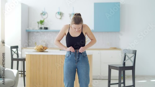 Young fat woman cannot wear small pants after gaining weight. An overweight female tries to button her jeans. Girl with belly getting dressed putting trousers on. Overweight trying to fasten too photo