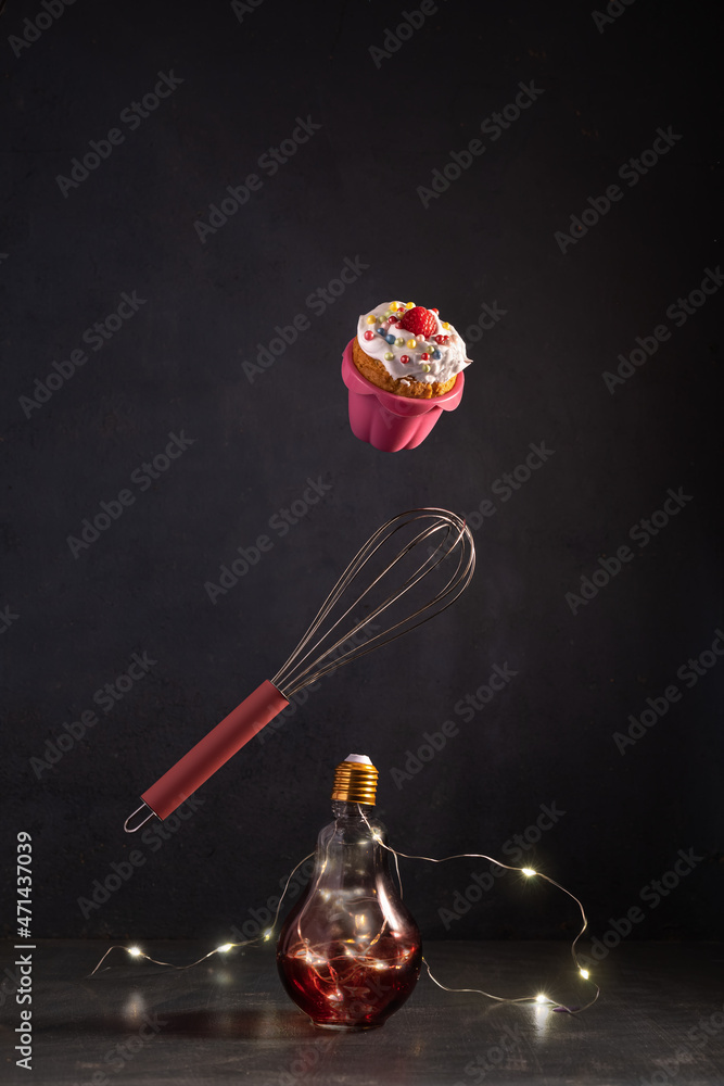 Flying in the air Easter or Christmas cupcake decorated with berries, Christmas lamps illumination and whisk for mixing products Flying in the air Easter or Christmas cupcake decorated with berries, Christmas lamps illumination and whisk for mixing products