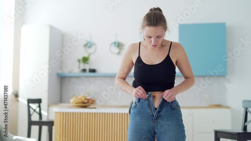 Young fat woman cannot wear small pants after gaining weight. An overweight female tries to button her jeans. Girl with belly getting dressed putting trousers on. Overweight trying to fasten too photo