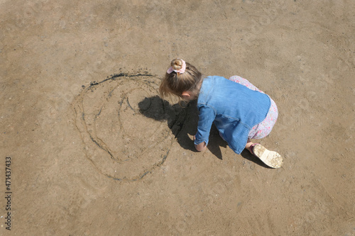 Blond kid girl writing in the sand with blue shirt