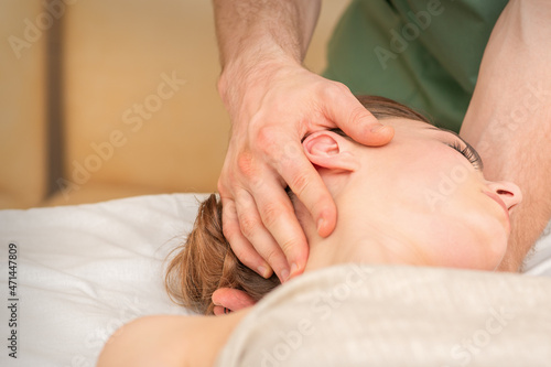 Osteopath doing massage on the female head in rehabilitation clinic center