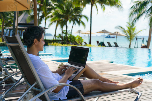 Fototapeta Asian man spent his summer vacation working on his laptop in a chair near the swimming pool in resort hotel near sea