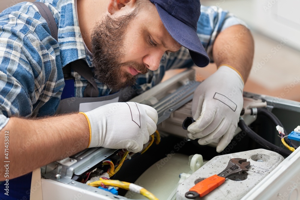 a man repairing a washing machine in cap a man repairing a washing machine in cap
