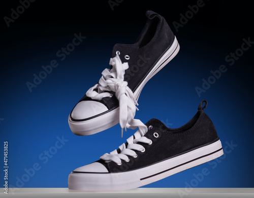 Black sneakers classic vintage shoe stylish shot. Levitating in air with tie their laces on a dark blu background with copy space