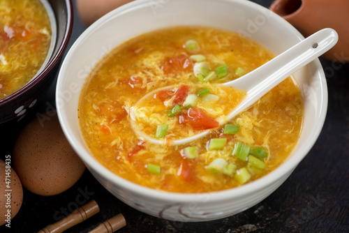 Closeup of chinese tomato egg-drop soup topped with scallions and served in a beige bowl, selective focus
