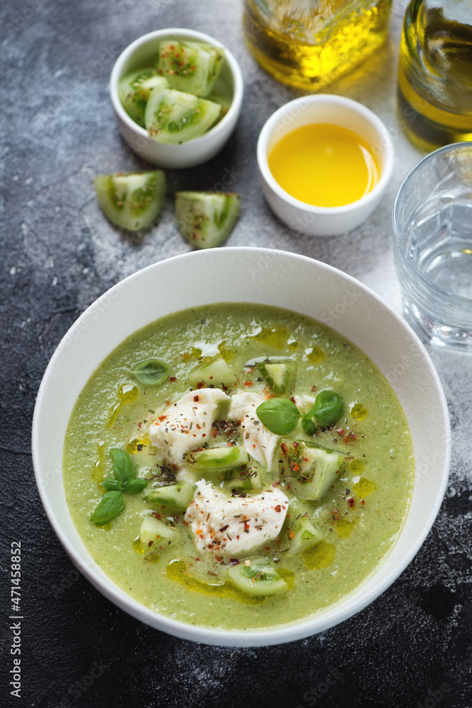 Green tomato gazpacho served with mozzarella cheese in a white bowl, vertical shot on a dark-grey stone background