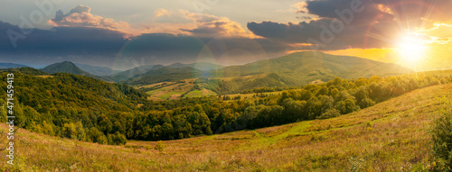 carpathian countryside in september at sunset. beautiful mountain landscape with grassy field on rolling hill in evening light. rural scenery with village in the distant valley. clouds on the sky