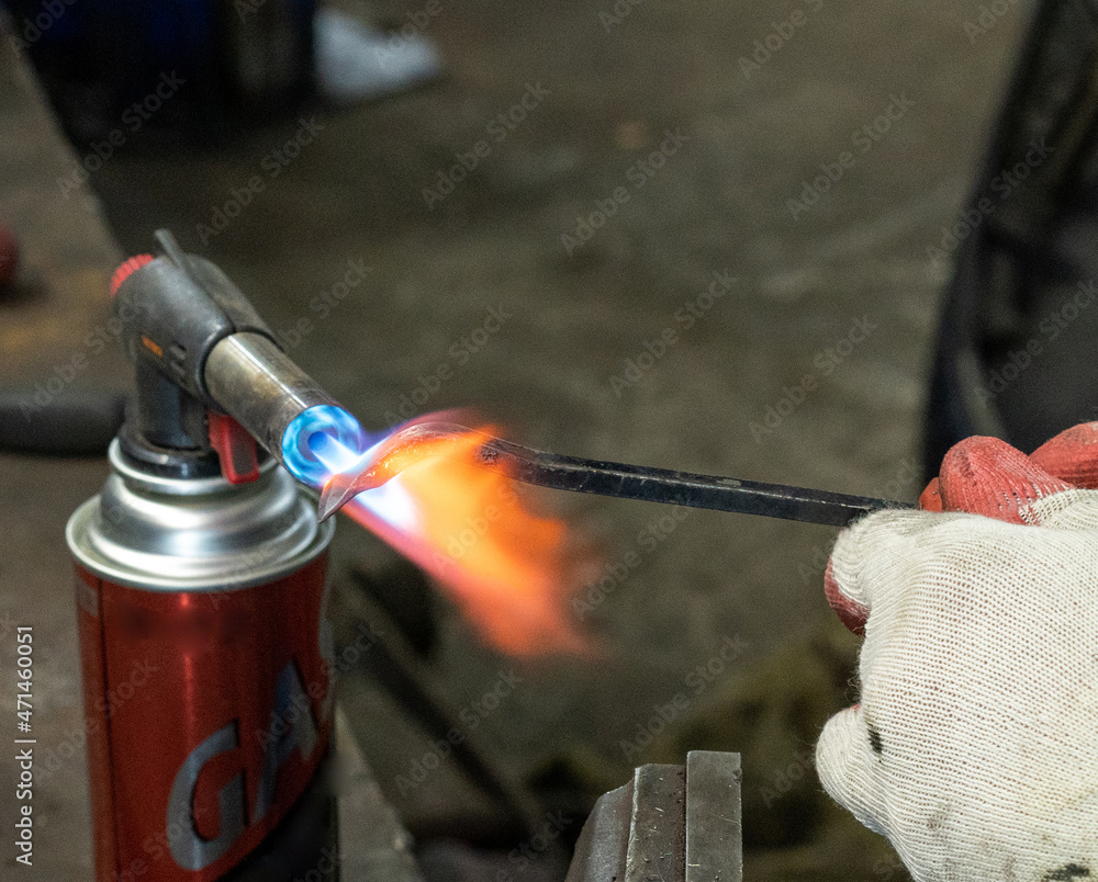 Naklejka premium Photo of a gas burner and metal melting. Male hands in work gloves in the garage