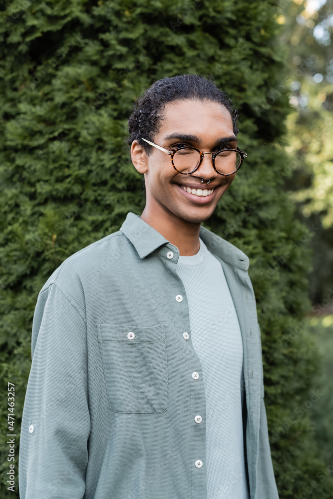 young african american man in grey shirt, eyeglasses and piercing smiling at camera outdoor young african american man in grey shirt, eyeglasses and piercing smiling at camera outdoor