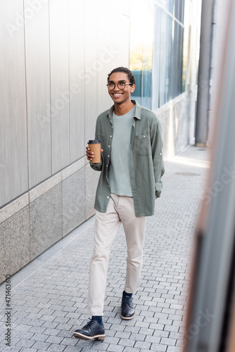 full length view of young and stylish african american man walking on street with coffee to go
