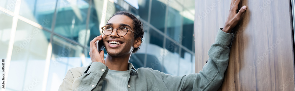 joyful african american man looking away while talking on mobile phone outdoors, banner joyful african american man looking away while talking on mobile phone outdoors, banner