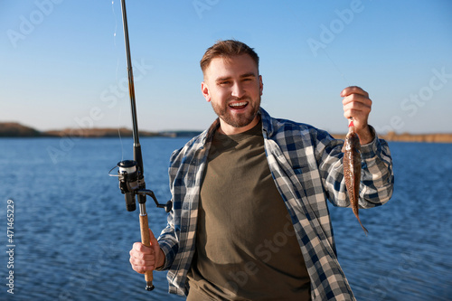 Fisherman holding fishing rod and catch at riverside