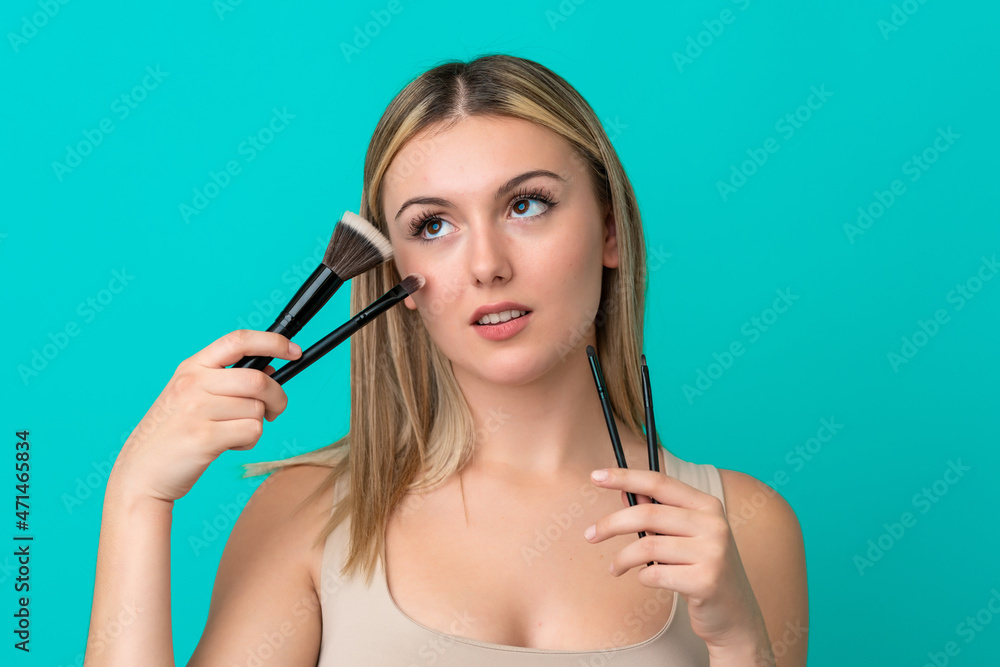 Young caucasian woman isolated on blue background holding makeup brush Young caucasian woman isolated on blue background holding makeup brush