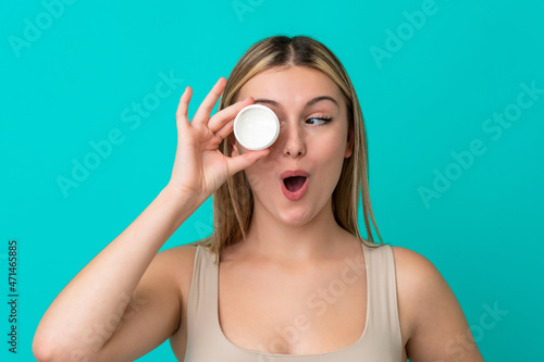 Young caucasian woman isolated on blue background with moisturizer and surprised