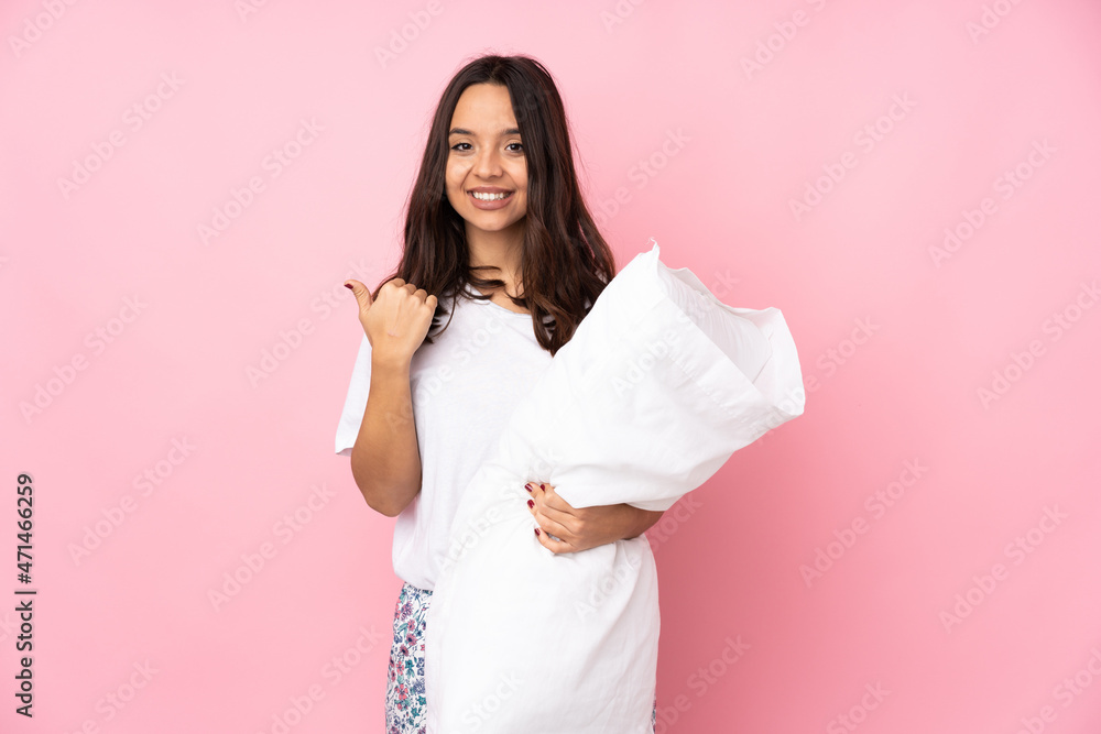 Young woman in pajamas isolated on pink background pointing to the side to present a product Young woman in pajamas isolated on pink background pointing to the side to present a product