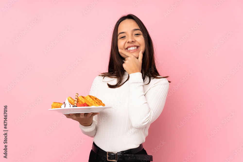 Young brunette woman holding waffles over isolated pink background smiling Young brunette woman holding waffles over isolated pink background smiling