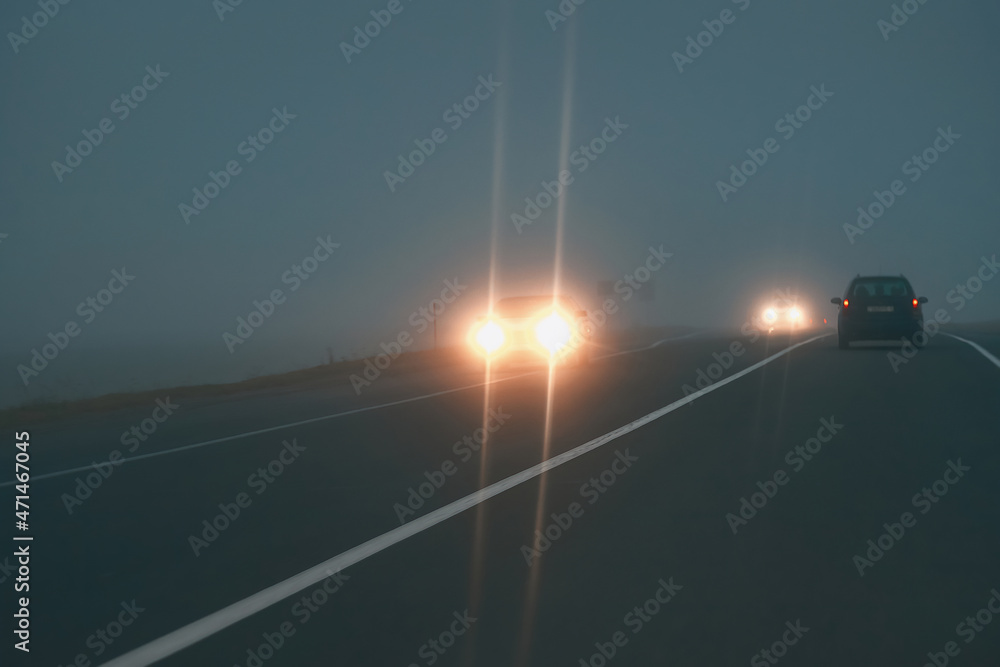 Headlights of oncoming cars driving in fog. Driving in fog, car headlights at foggy evening. - obrazy, fototapety, plakaty 