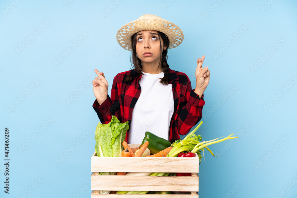 Young farmer Woman holding fresh vegetables in a wooden basket with fingers crossing and wishing the best
