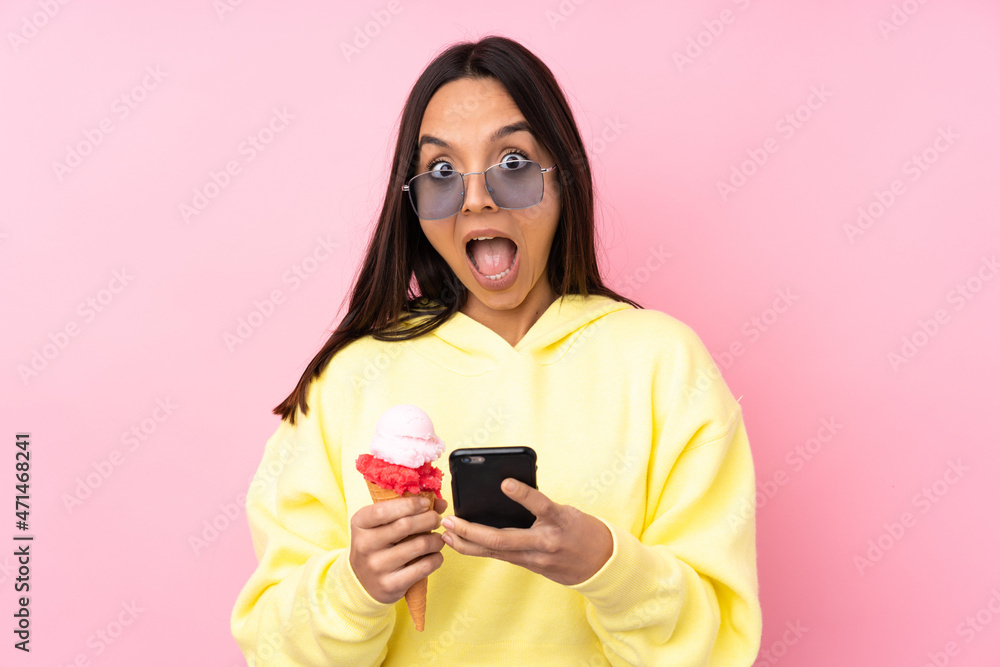 Young brunette girl holding a cornet ice cream over isolated pink background surprised and sending a message Young brunette girl holding a cornet ice cream over isolated pink background surprised and sending a message