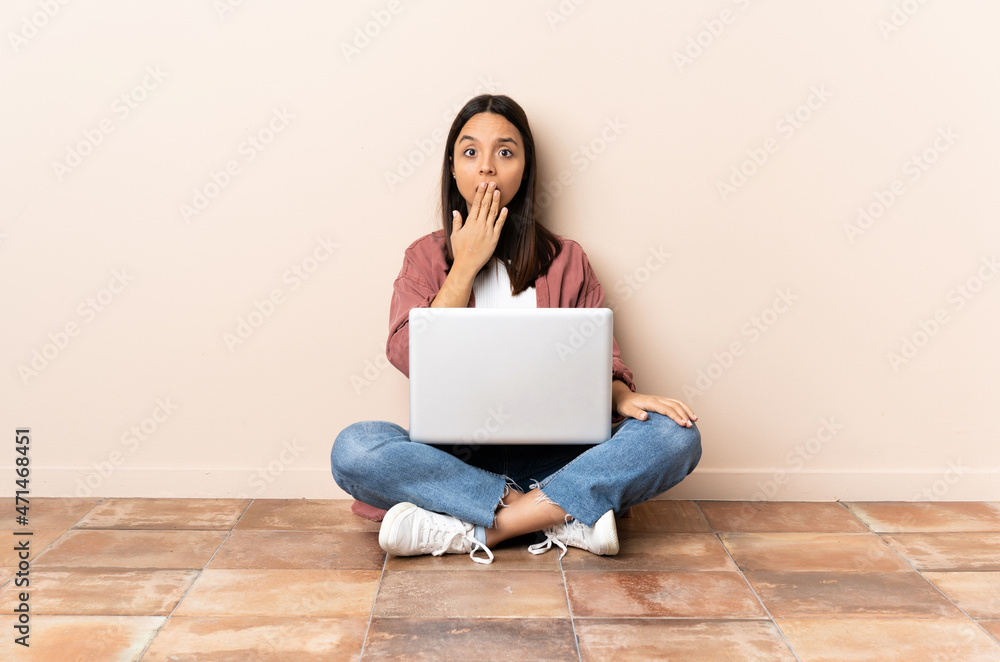 Young mixed race woman with a laptop sitting on the floor covering mouth with hand Young mixed race woman with a laptop sitting on the floor covering mouth with hand
