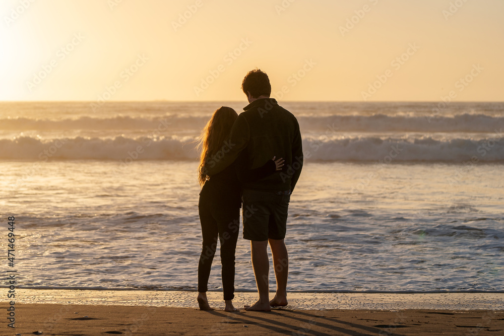 young couple in love hug each other on the beach watching the sunset, back view