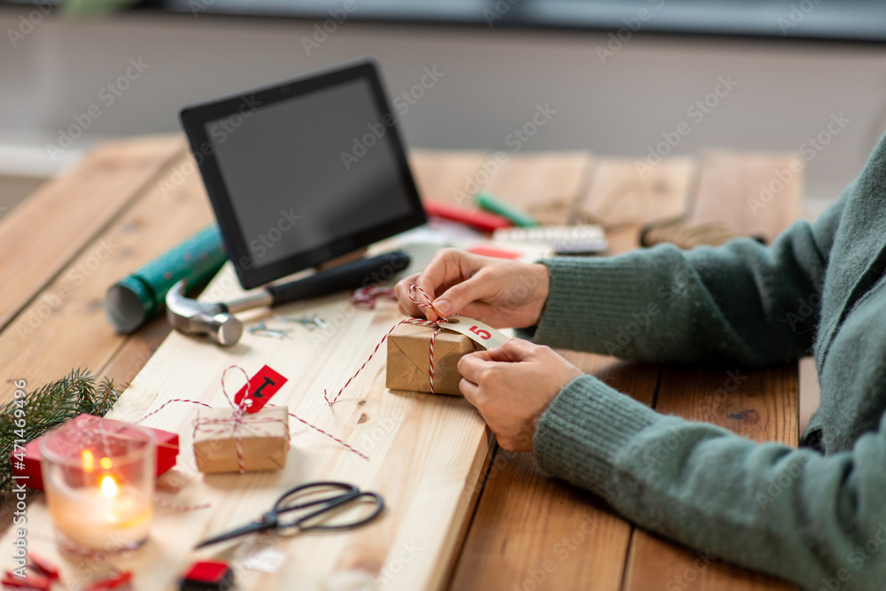 winter holidays and hobby concept - close up of woman with tablet pc computer packing christmas gift or making advent calendar at home winter holidays and hobby concept - close up of woman with tablet pc computer packing christmas gift or making advent calendar at home