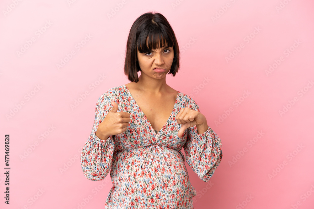 Young pregnant woman over isolated pink background making good-bad sign. Undecided between yes or not Young pregnant woman over isolated pink background making good-bad sign. Undecided between yes or not