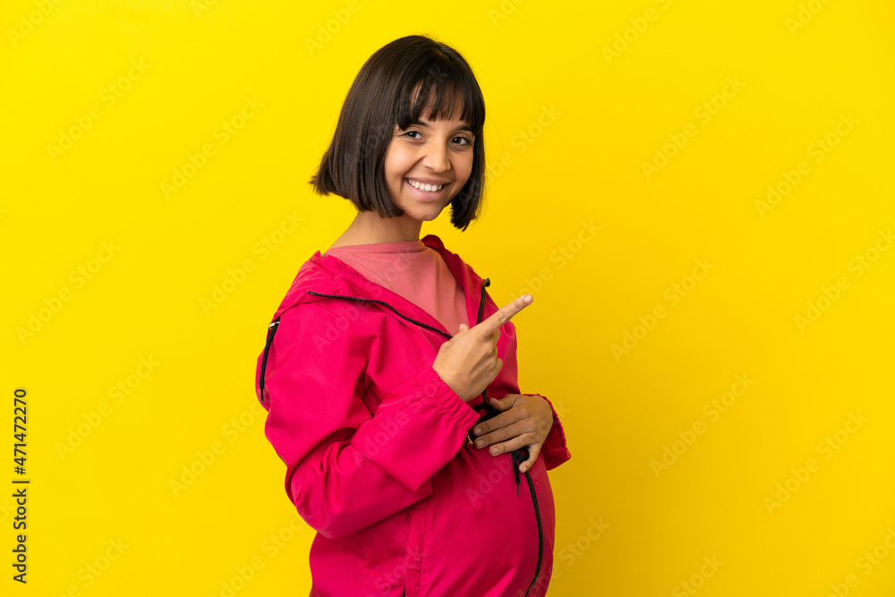 Young pregnant woman over isolated yellow background pointing to the side to present a product Young pregnant woman over isolated yellow background pointing to the side to present a product
