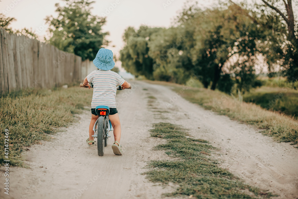 Fototapeta premium Baby boy rides a bicycle along the countryside. Back view. Autumn landscape. Healthy lifestyle.