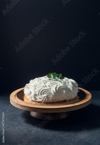 food, sweets and objects concept - close up of meringue or zephyr cake on wooden stand with eucalyptus branch over dark background