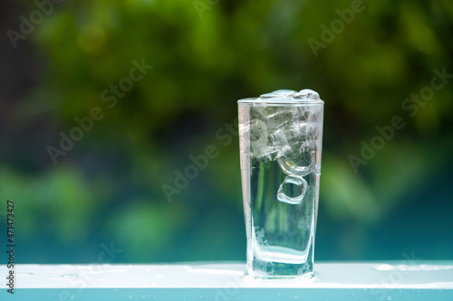 The glass of Cool fresh water drink with ice cube on the table in Green blurred background.