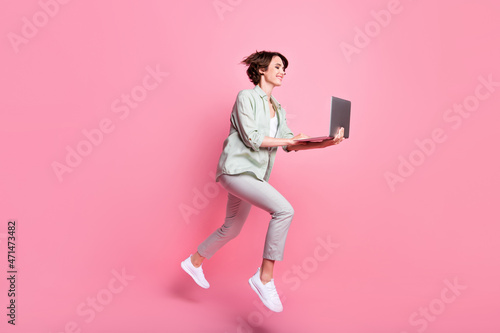 Full length profile photo of nice millennial lady jump with laptop wear grey green suit isolated on pink color background