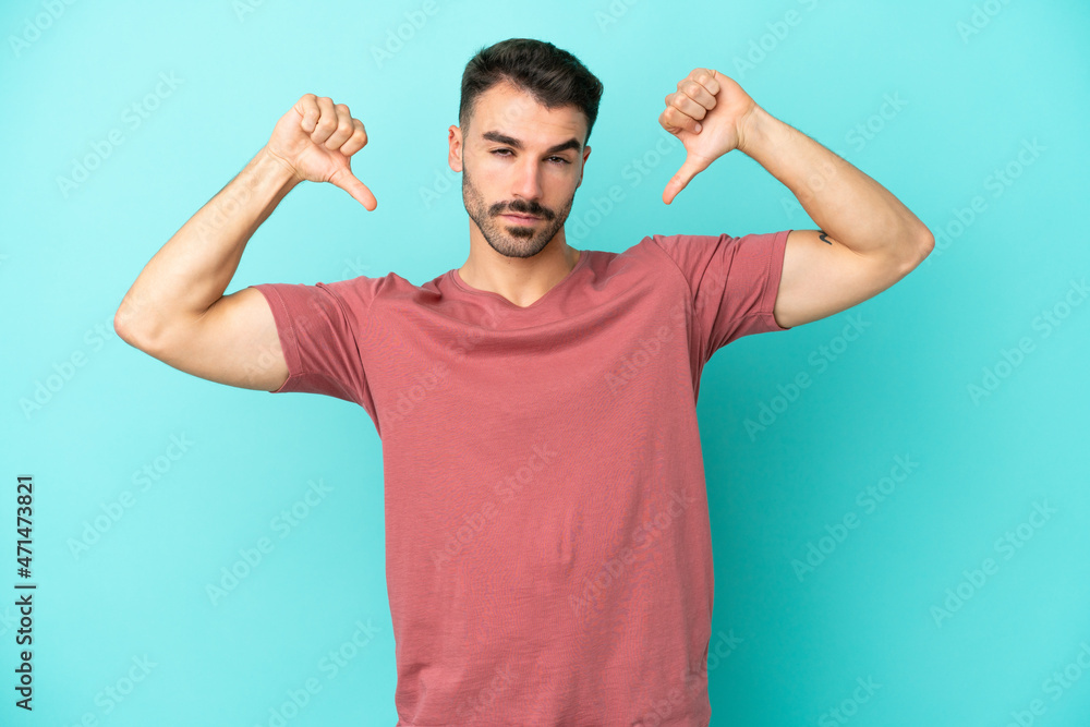 Young caucasian man isolated on blue background showing thumb down with two hands Young caucasian man isolated on blue background showing thumb down with two hands