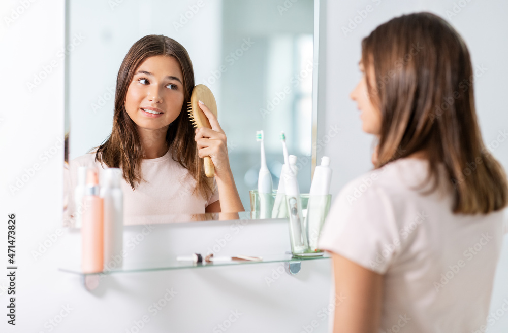 beauty and people concept - teenage girl looking to mirror and brushing wet hair with comb at home bathroom beauty and people concept - teenage girl looking to mirror and brushing wet hair with comb at home bathroom